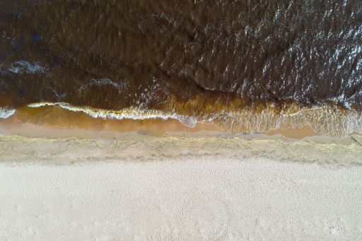 An aerial top view of the coastline separating sands and brownish wavy waters