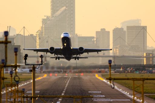 A plane taking off the runway with buildings and orange sky in the background