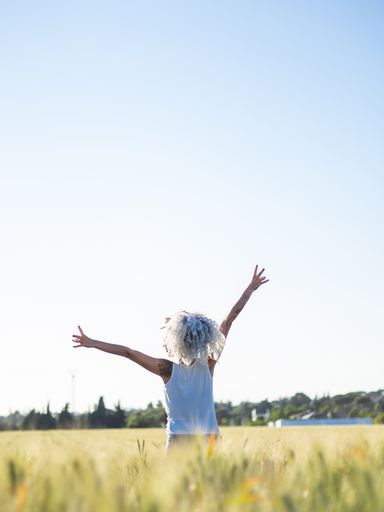 A cheerful woman with white curly hair and tattoos posing in a field on a sunny day in the countryside