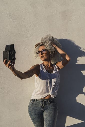 A vertical shot of a sexy Caucasian female posing outdoors while taking a selfie on an old camera