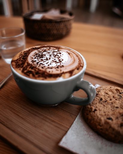 A vertical closeup shot of a cup of cappuccino and a cookie on a wooden surface