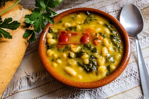 A top view shot of vegetable soup in the clay bowl with bread and greens on the table