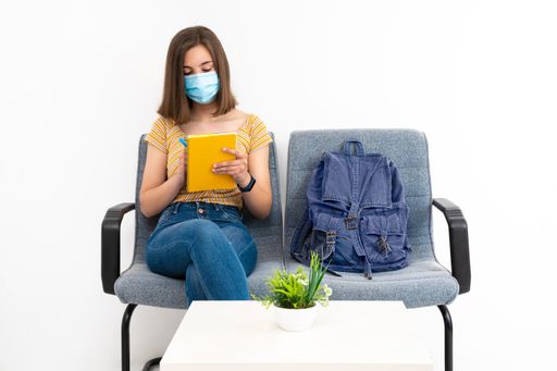 A young female client in the waiting room with a mask studying while waiting on a white background