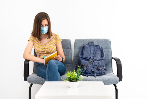 A young female client in the waiting room with a mask studying while waiting on a white background