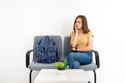 A worried young female client in the waiting room sitting on a gray chair on a white background