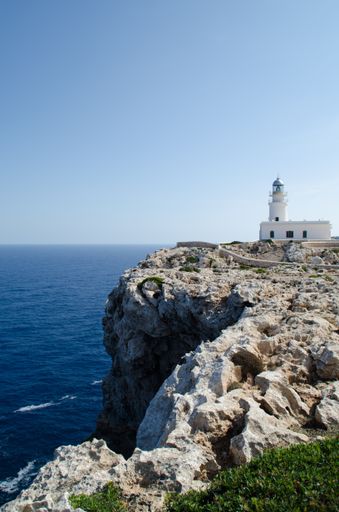 A vertical shot of a beautiful white lighthouse at the edge of a cliff in Menorca island, Spain