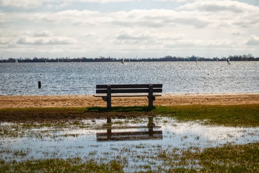 A wooden bench situated on a meadow, with the tranquil calm waters of a lake in the background.