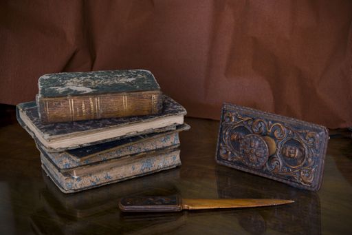 A view at a stack of ancient stained books by a metallic artifact and an old vintage knife