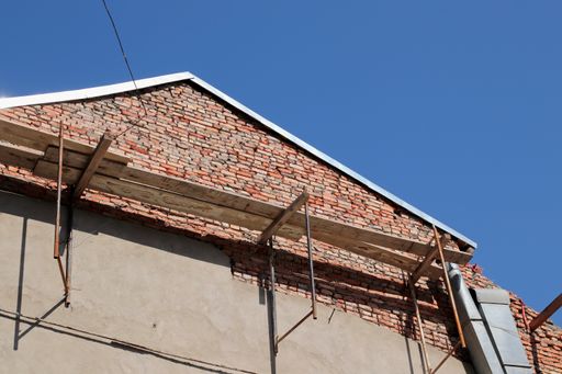 A low angle shot of the roof and wall of a brick house under construction with a blue sky