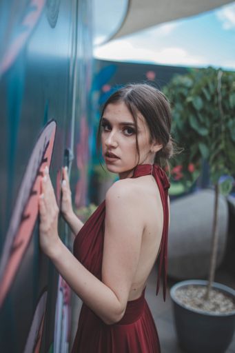 A shallow focus of a cheerful woman wearing a red dress and posing against a wall of an outdoor cafe