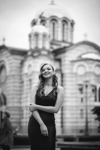A grayscale portrait of an elegant Caucasian woman wearing a long black dress outdoors