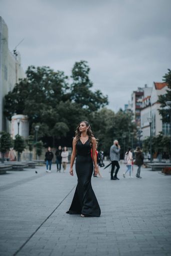 A vertical shot of beautiful sexy Caucasian woman in a black backless gown posing outdoors