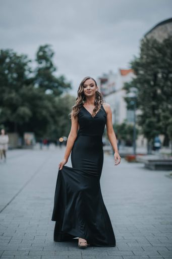 A full body shot of a beautiful elegant woman in a fancy black dress walking outside holding her skirt