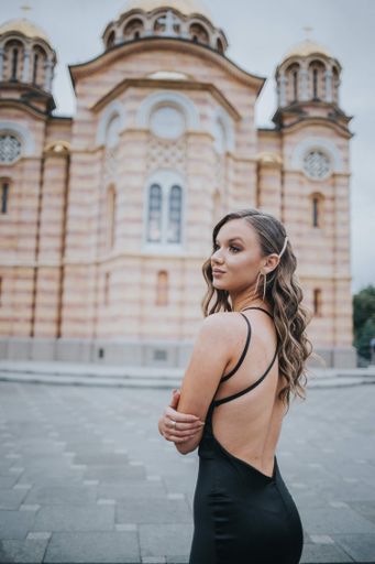 An attractive Caucasian female wearing a beautiful long black dress posing on a street