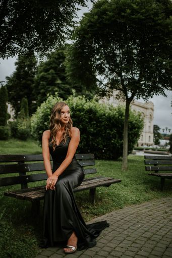 A vertical shot of a Caucasian sexy woman with a black evening dress sitting on the garden bench
