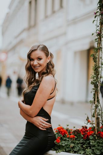 An attractive Caucasian female wearing a beautiful long black dress posing on a street near flowers