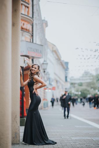 A full body shot of a beautiful elegant smiling woman in a fancy black dress posing outside in summer