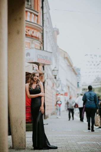 A vertical shot of a Caucasian sexy woman with a black evening dress leaning on the street columns