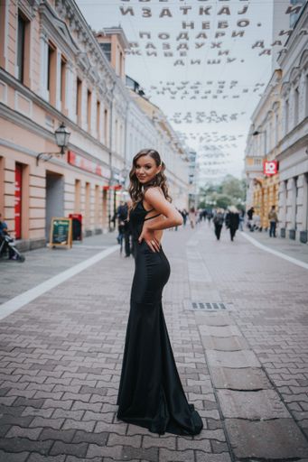 A vertical shot of beautiful sexy Caucasian woman in a black backless gown posing at outdoors