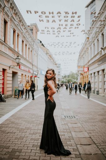 A beautiful sexy Caucasian woman in a black backless gown posing outdoors