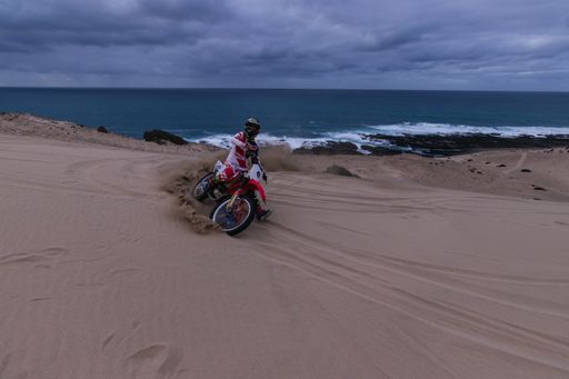 A professional motorcycle driver driving on a sandy seashore
