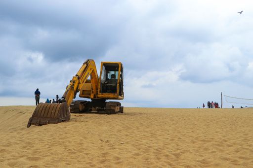 A closeup shot of a bulldozer working on the seashore against a blue sky backgrou