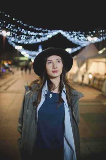 A shallow focus shot of a young beautiful Caucasian female in a black hat walking in the night city