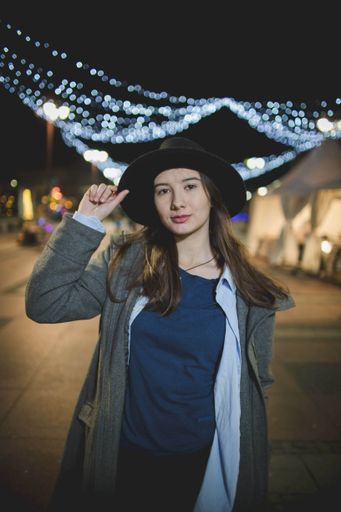A shallow focus shot of a young beautiful Caucasian female in a black hat posing at camera