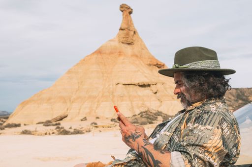 A male traveler looking at his cell phone in the desert landscape of Bardenas Reales, Arguedas, Navarra, Spain