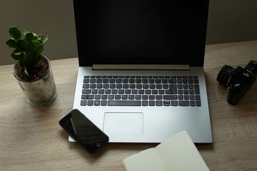 A laptop, an open notebook, a cellphone, and a plant on an office table