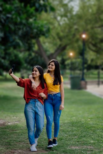 Two gorgeous cheerful young girlfriends from Argentina taking a selfie in a park in the evening