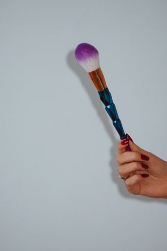 A vertical shot of female hands holding a colorful makeup brush on a clear background