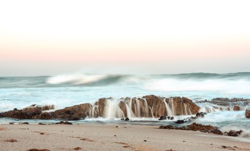A beautiful shot of the waves of the ocean crashing into the rock formation by the shore