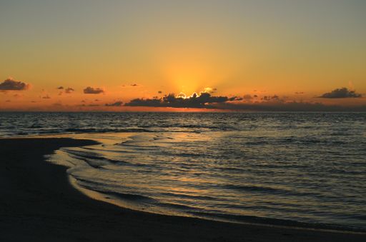 A breathtaking sunset view from a beach with low tides and golden sun hiding behind clouds