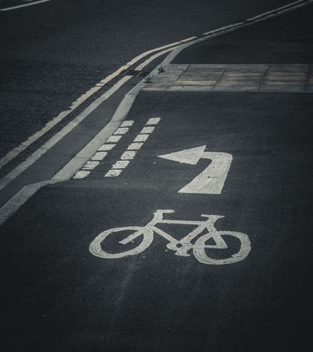 An urban scene with a bicycle lane with a white arrow painted on the side of the road