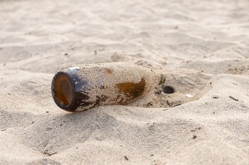 A closeup of an empty glass bottle of beer lying on a beach