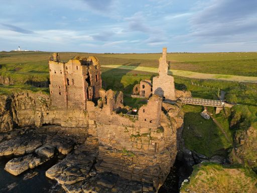 An aerial view of the historic Sinclair Girnigoe Castle ruins on a rocky outcrop at sunset