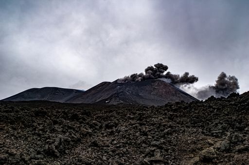 A beautiful view of a volcano erupting smoke under a gloomy sky