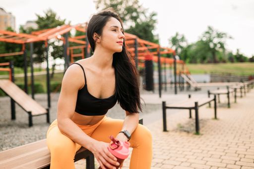 A Sporty brunette young woman drinks water after training outdoors. on the sports field