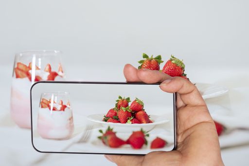 A male hand taking a photo of fresh strawberries on a white plate with a glass of panna cotta