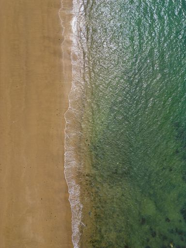 A drone shot of a beach in the United Kingdom with a top-down view, showing the shore and the ocean