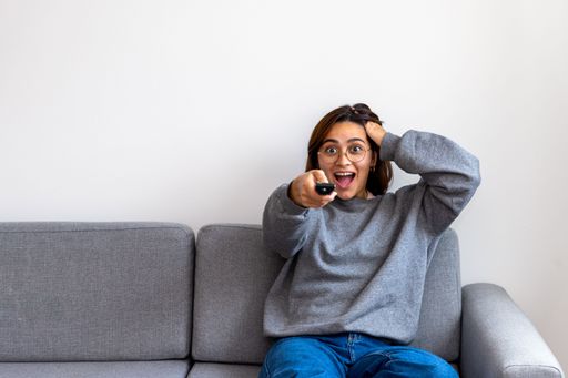 a black-haired woman in gray sweatshirt watching tv surprised