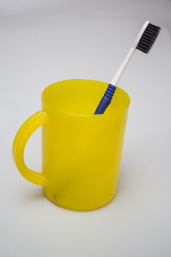 A vertical shot of a toothbrush in a yellow plastic mug with a white color in the background