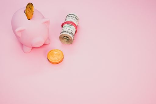 A closeup of a piggy bank with coins next to a roll of dollars isolated on pink background