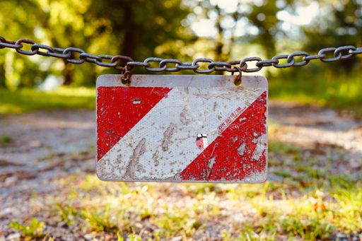 A closeup shot of a red and white damaged warning sign hanging on a chain in the park