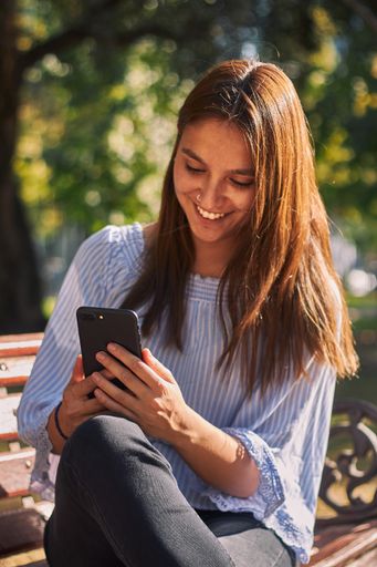 A vertical shot of a girl sitting on the bench and looking at her phone