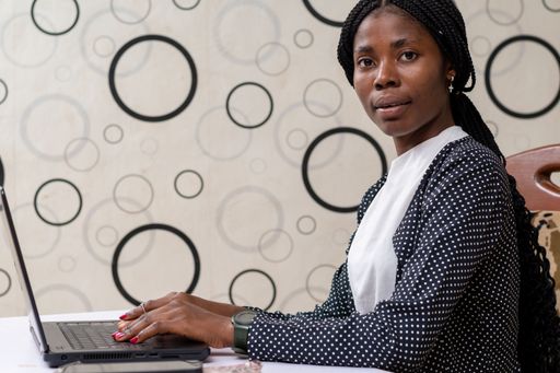 A Nigerian worker looking at the camera while sitting by her desk in the office