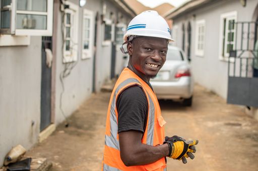 A content male construction worker smiles while wearing a protective hard hat and safety vest, in an outdoor environment