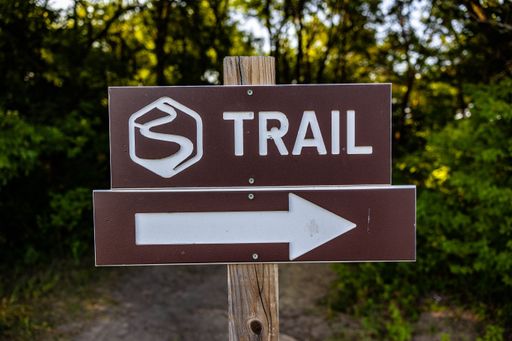 A closeup of a sign with the word "trail" and an arrow