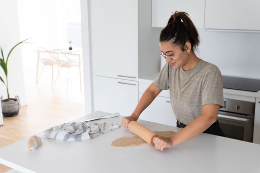 a young black haired woman cooking happy homemade pasta by hand with rolling pin